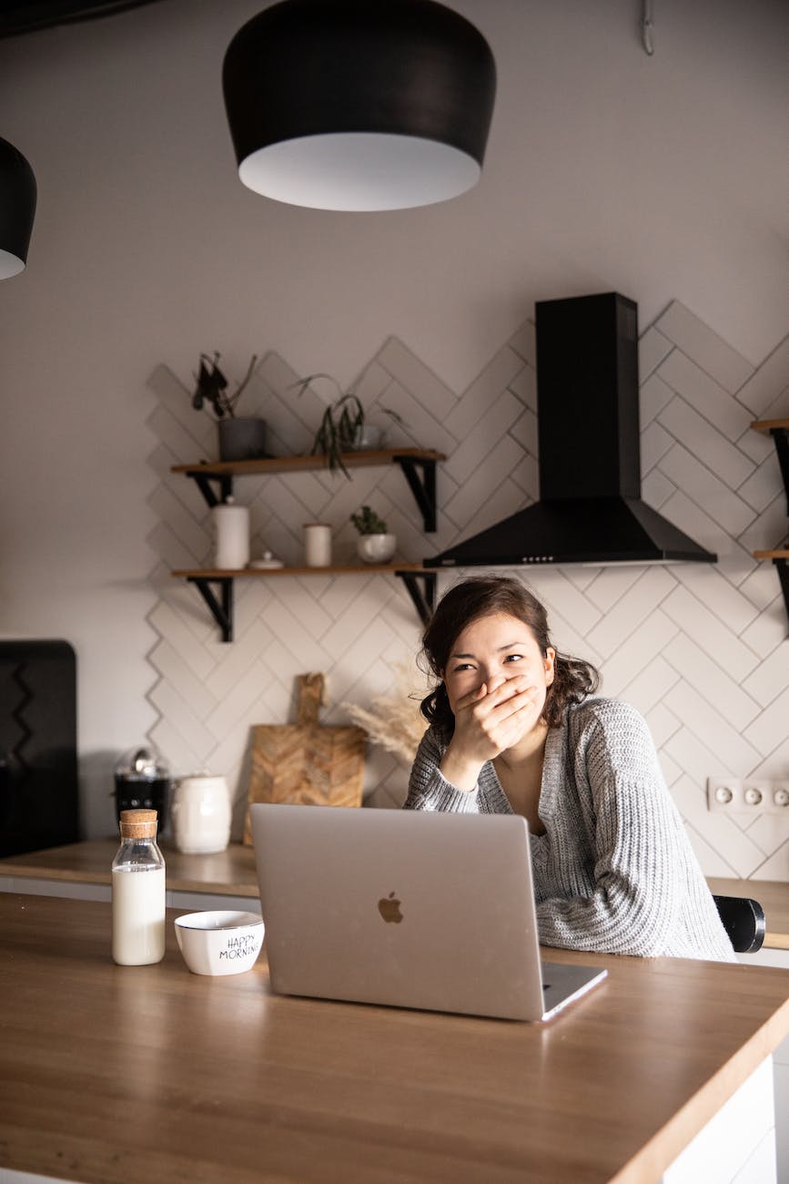 cheerful woman with laptop laughing in modern kitchen