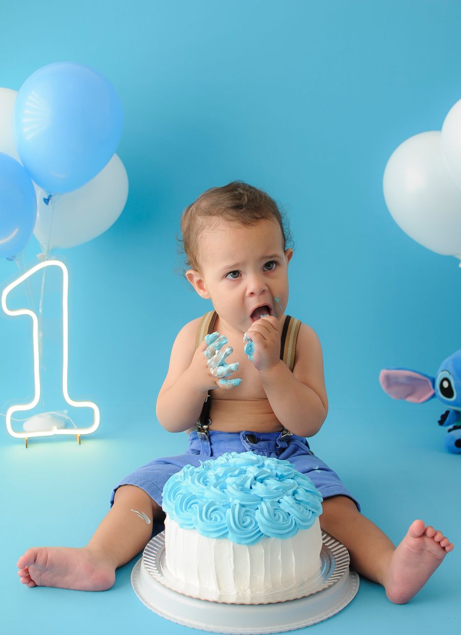 a baby boy sitting on a blue cake with a blue balloon and a blue balloon