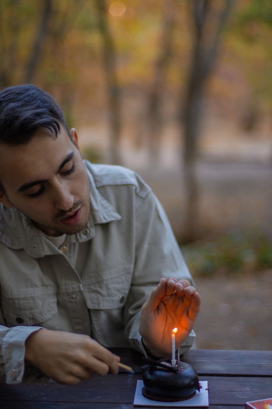 young man lighting candle on a cake outdoors