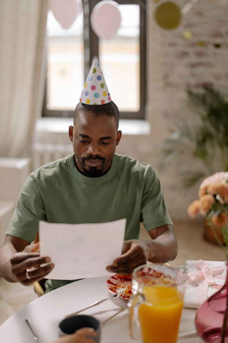 photograph of a man with a party hat holding a piece of paper