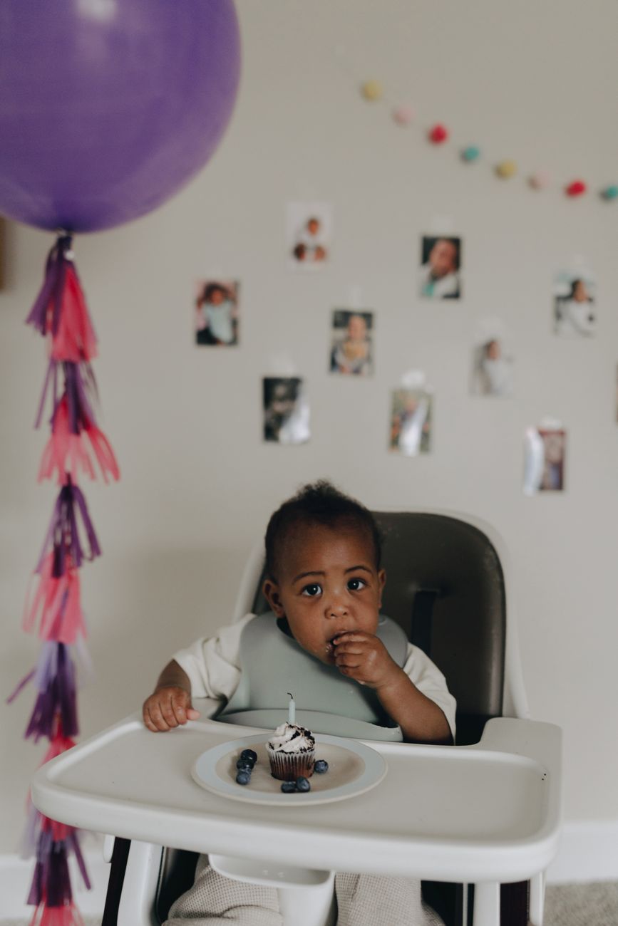 baby sitting in a high baby chair and eating a cupcake at the first birthday party