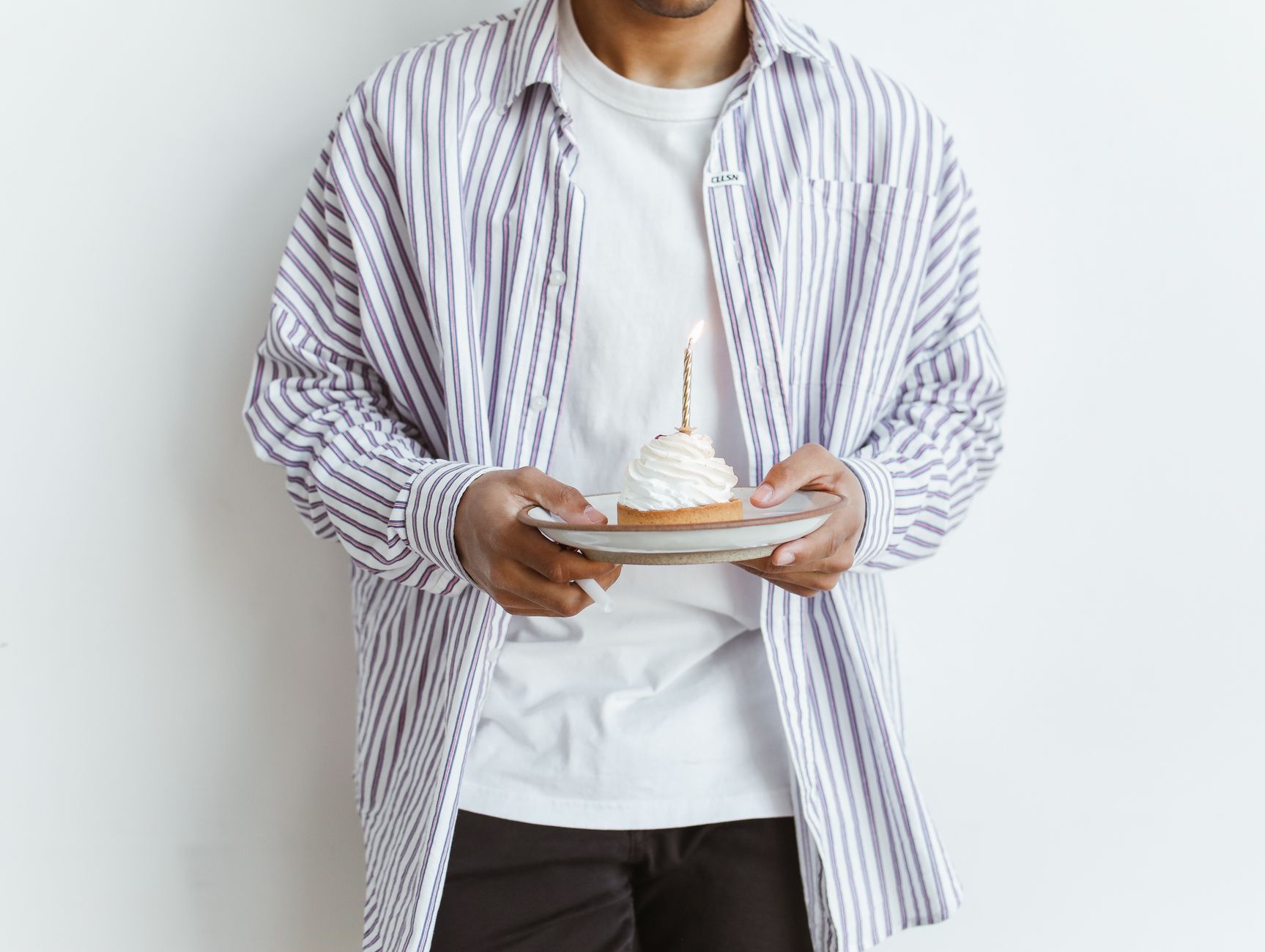 person in striped long sleeve shirt holding white ceramic plate with cake